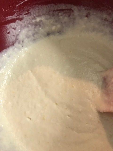 A close-up of thick, creamy parker house rolls batter in a red mixing bowl, with a spatula partially visible on the right side.