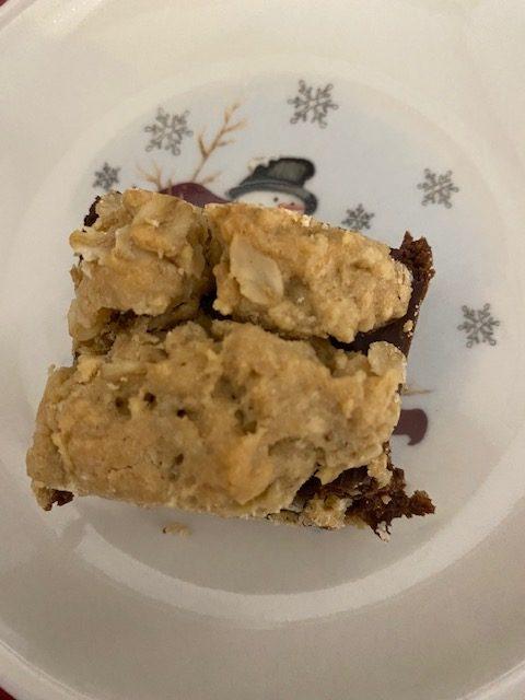 A close-up of fudge nut bars with a crumbly oat topping and a chocolate layer, served on a white plate decorated with snowflakes and a snowman.