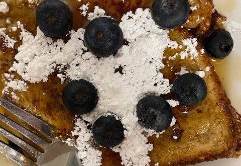 French toast with syrup, powdered sugar, and blueberries on white plate.