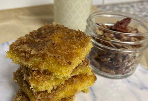 Pecan Cake Bars stacked on marble plate with cup of pecans and glass of milk in background