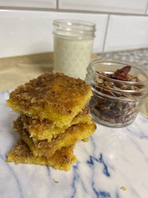Pecan Cake Bars stacked on marble plate with cup of pecans and glass of milk in background