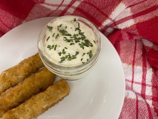 Tartar sauce in glass dish on white plate with fish sticks