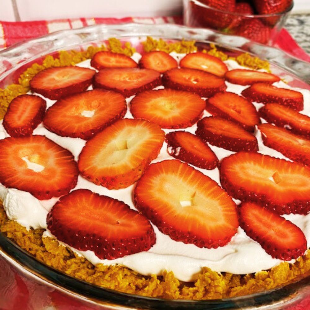 Close up of strawberry cream pie with bowl of strawberries in background
