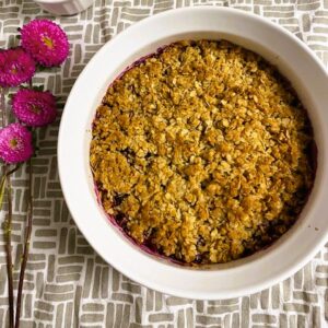 Blueberry Crisp in round dish next to pink flowers.
