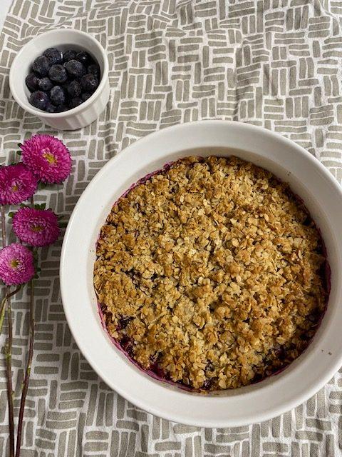 Blueberry Crisp in white casserole dish next to cup of blueberries