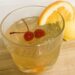 Whiskey Sour in clear glass with 2 maraschino cherries and orange slice.