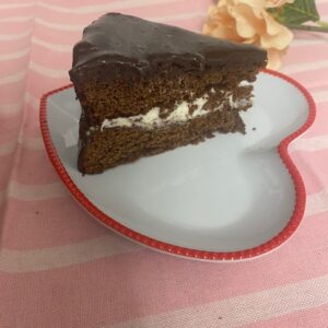 Slice of Old Fashioned Chocolate Cake on white heart-shaped plate on pink placemat.