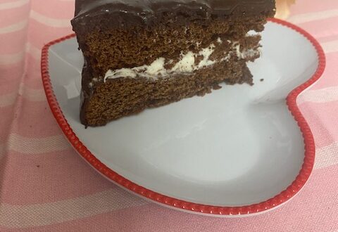 Slice of Old Fashioned Chocolate Cake on white heart-shaped plate on pink placemat.