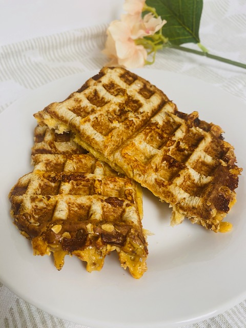 Waffle Grilled Cheese on white plate with pink flower in background.