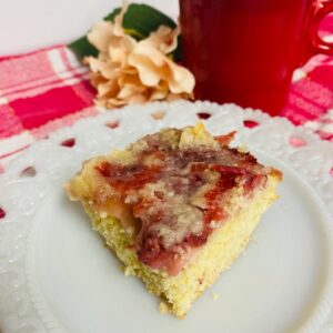 Strawberry Coffee Cake on white plate with red mug and pink flower in background.