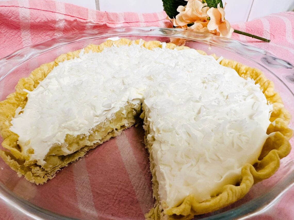 Coconut Cream Pie in glass pan with one slice missing.