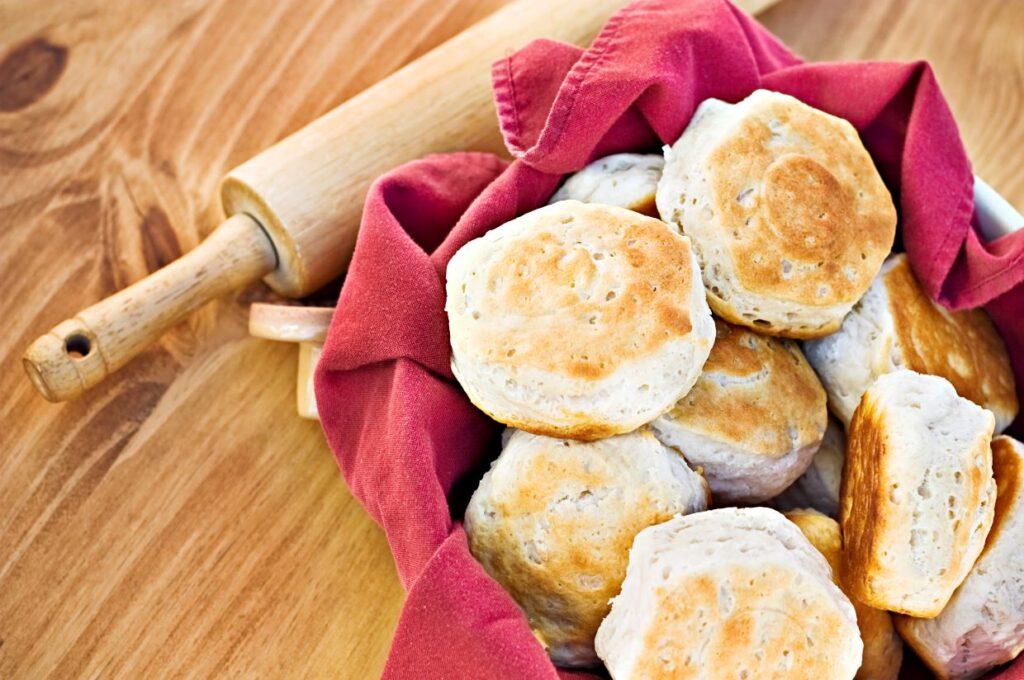 Buttermilk biscuits on red towel next to rolling pin.