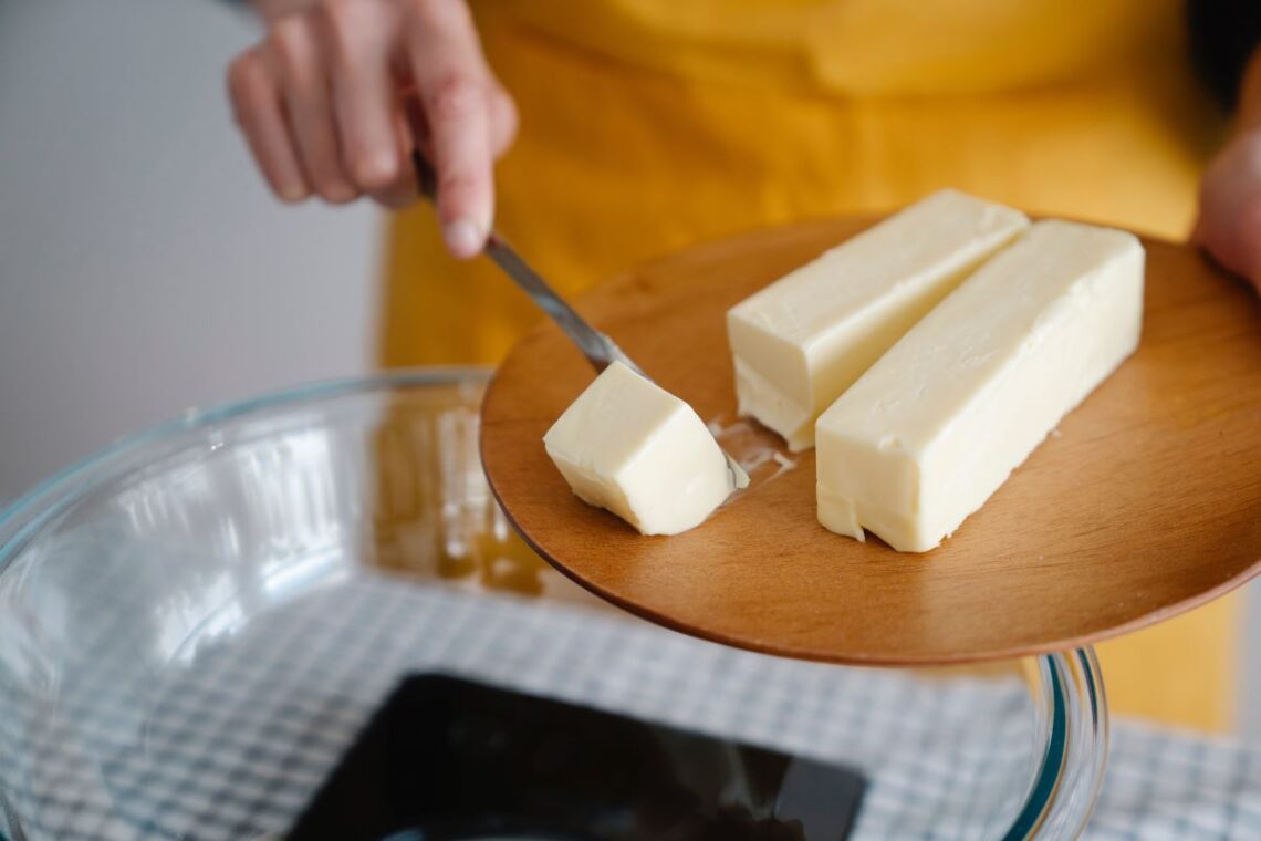Person adding block of butter to glass dish.