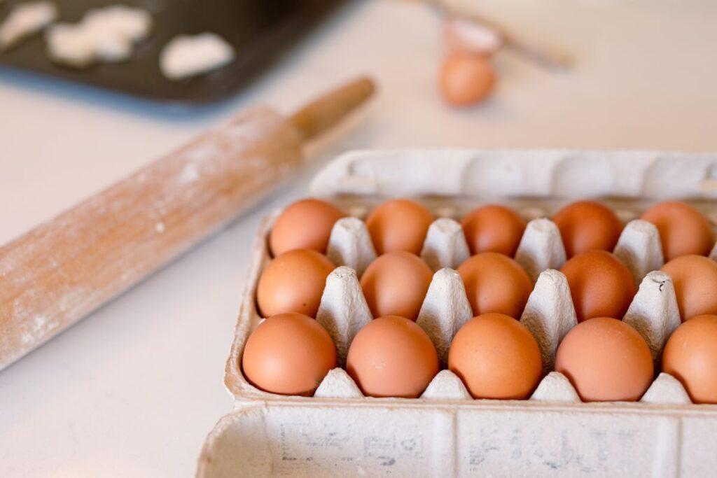 Eggs in carton on counter with rolling pin in background.