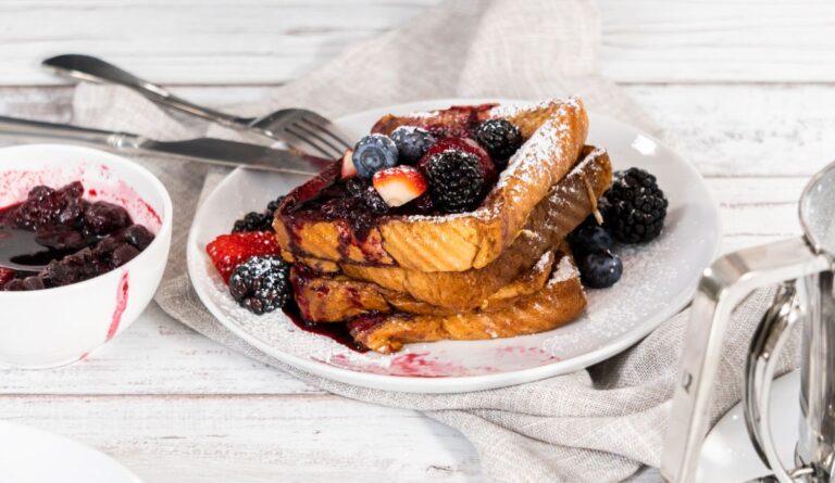 Stack of French toast on white plate with berries on top.