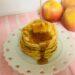 Stack of apple pancakes with butter and syrup on white plate.
