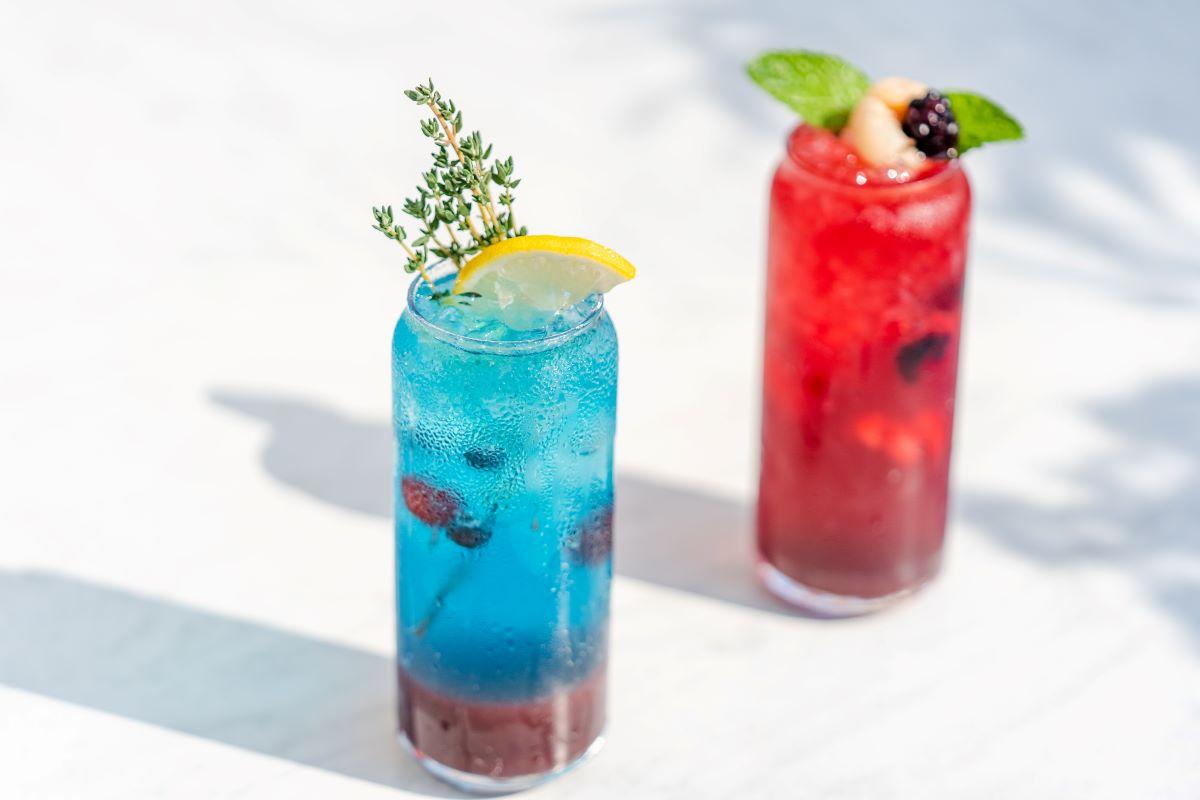 Blue cocktail in front of red cocktail on white table.