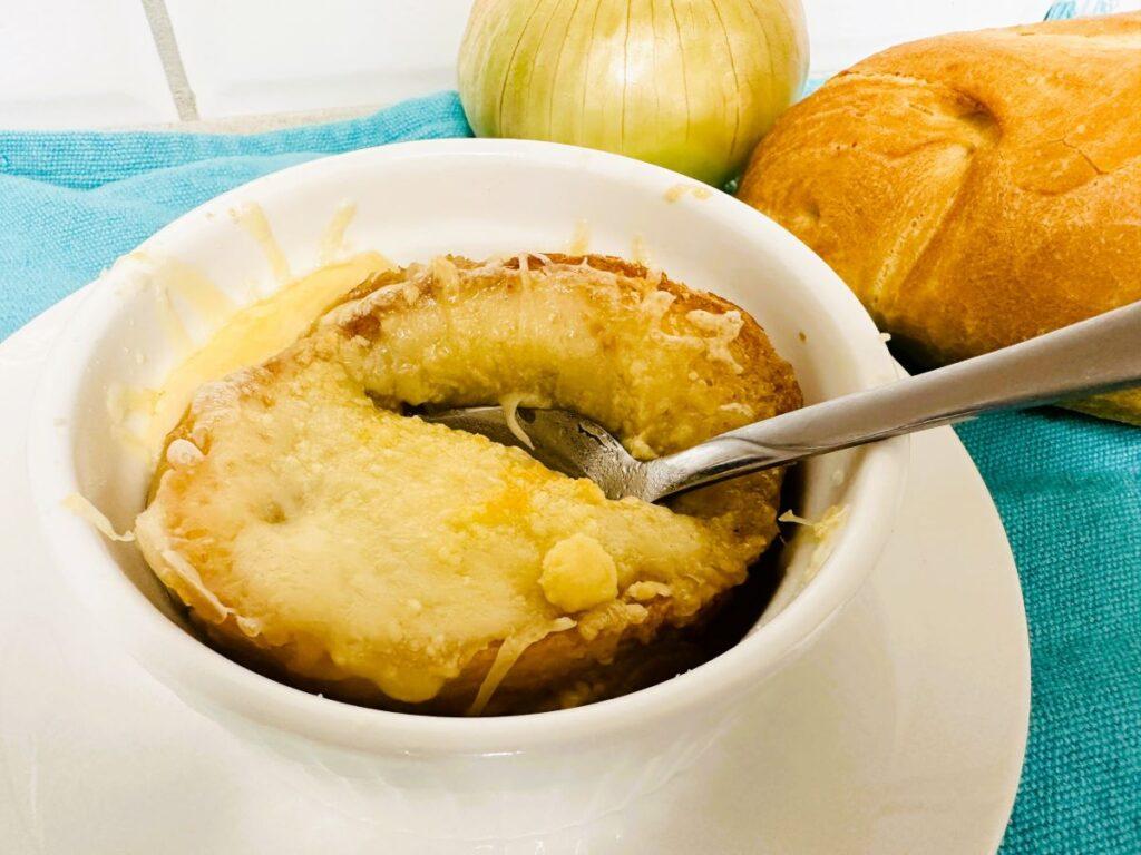 French onion soup with bread and cheese on top in white bowl.