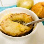 French onion soup with bread and cheese on top in white bowl.