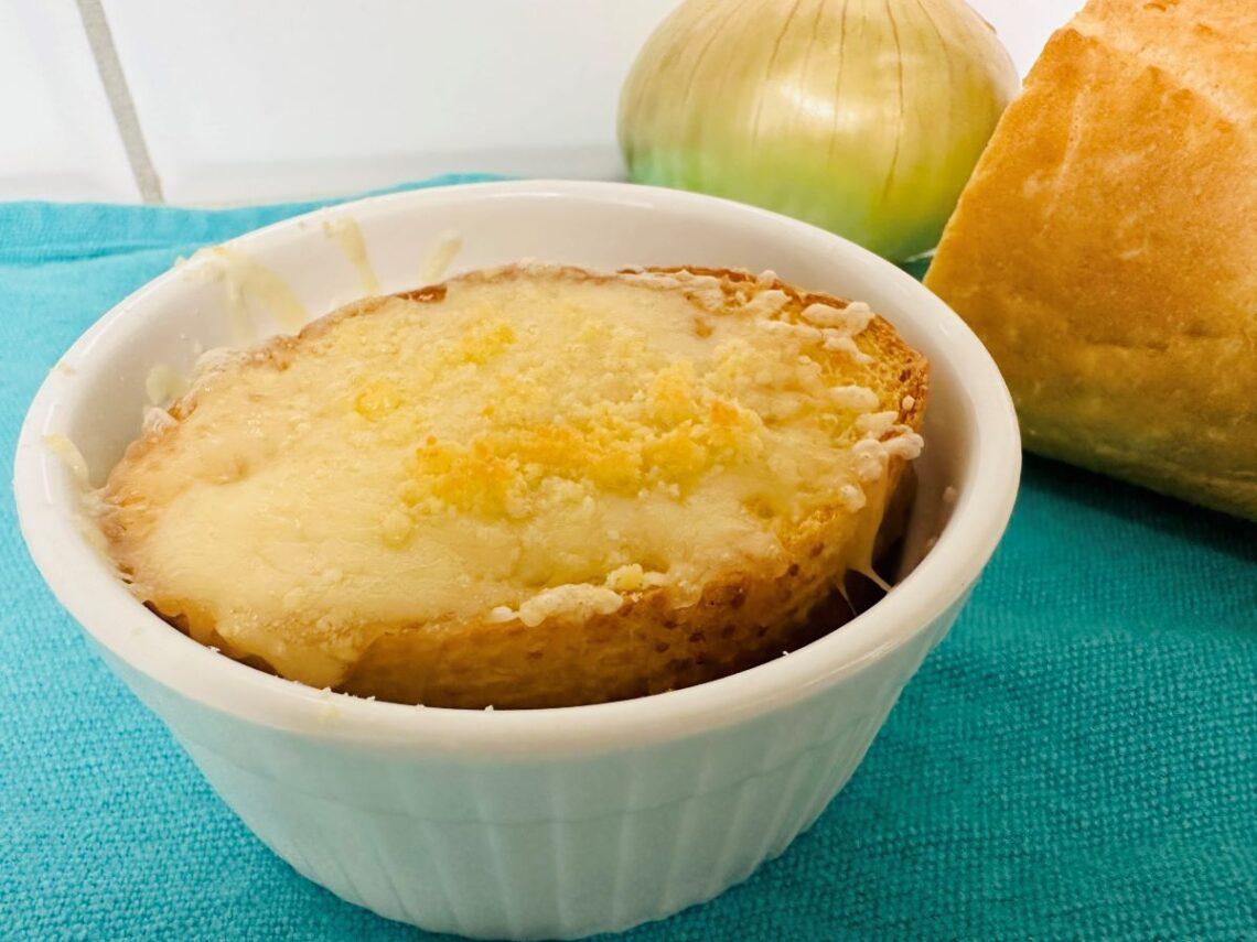 French onion soup with bread and melted cheese on top in white bowl.