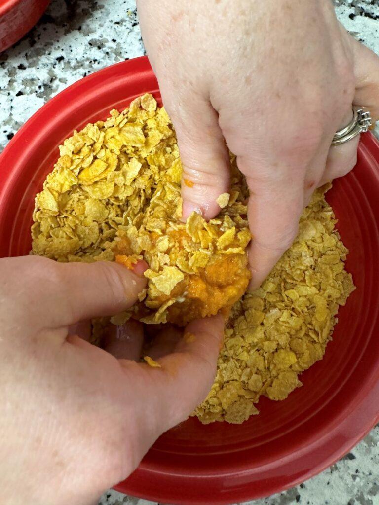 Hands rolling sweet potato puff in Corn Flake crumbs.