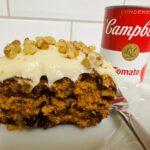 Slice of tomato soup cake with cream cheese frosting and walnuts on white plate.
