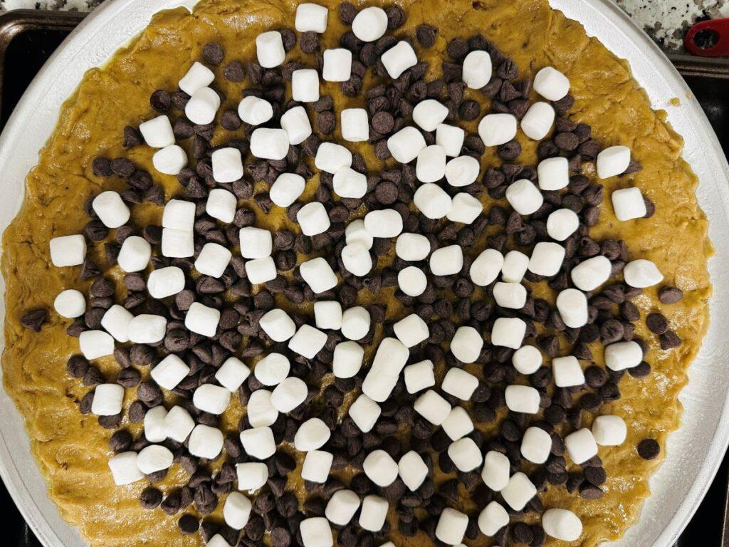 Chocolate chip dessert pizza with chocolate chips and marshmallows before baking.