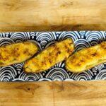 Three stuffed baked potatoes with a golden, seasoned top are arranged on a rectangular plate with a bold black and white geometric pattern, set on a wooden surface.