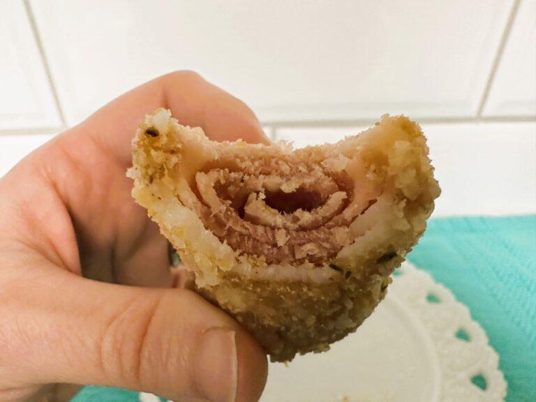 Hand holding breaded bacon curl with bite taken out of it.