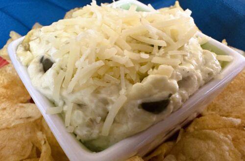 White dip in square white bowl surrounded by potato chips.