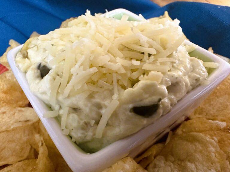 White dip in square white bowl surrounded by potato chips.
