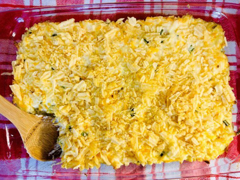 Rectangular glass pan with cheesy casserole topped with crushed potato chips.