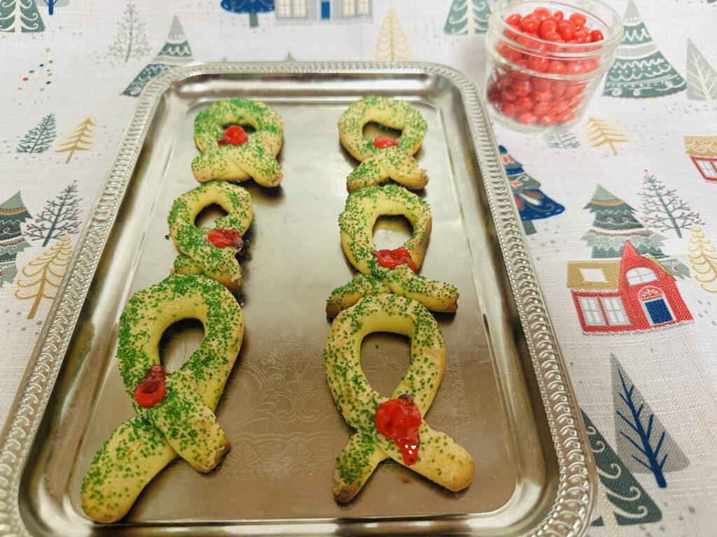 Wreath-shaped cookies with green sprinkles and round red candies on silver tray.