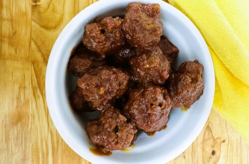 Cooked meatballs in white bowl on wooden board.