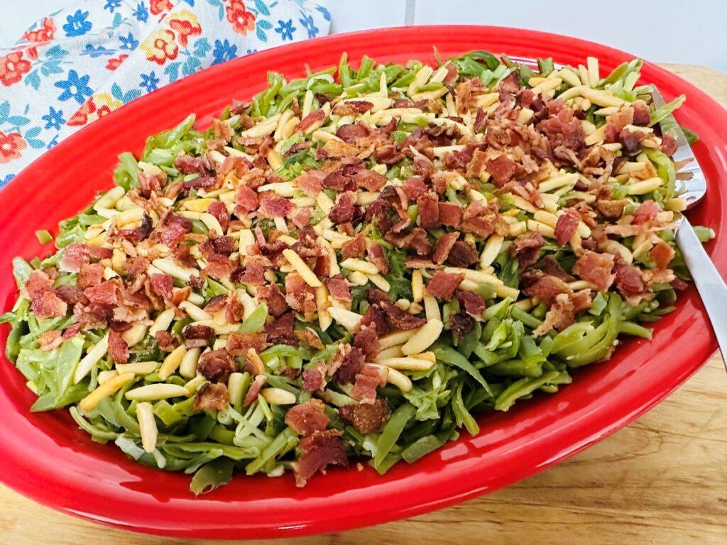 Green beans with slivered almonds and bacon on top in red dish.