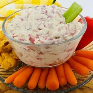 White dip in glass dish surrounded by cut vegetables.