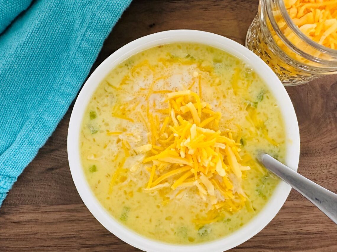 Yellow chowder with shredded cheese in white bowl.