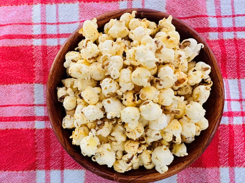 Top view of popcorn in wooden bowl on red gingham tablecloth.