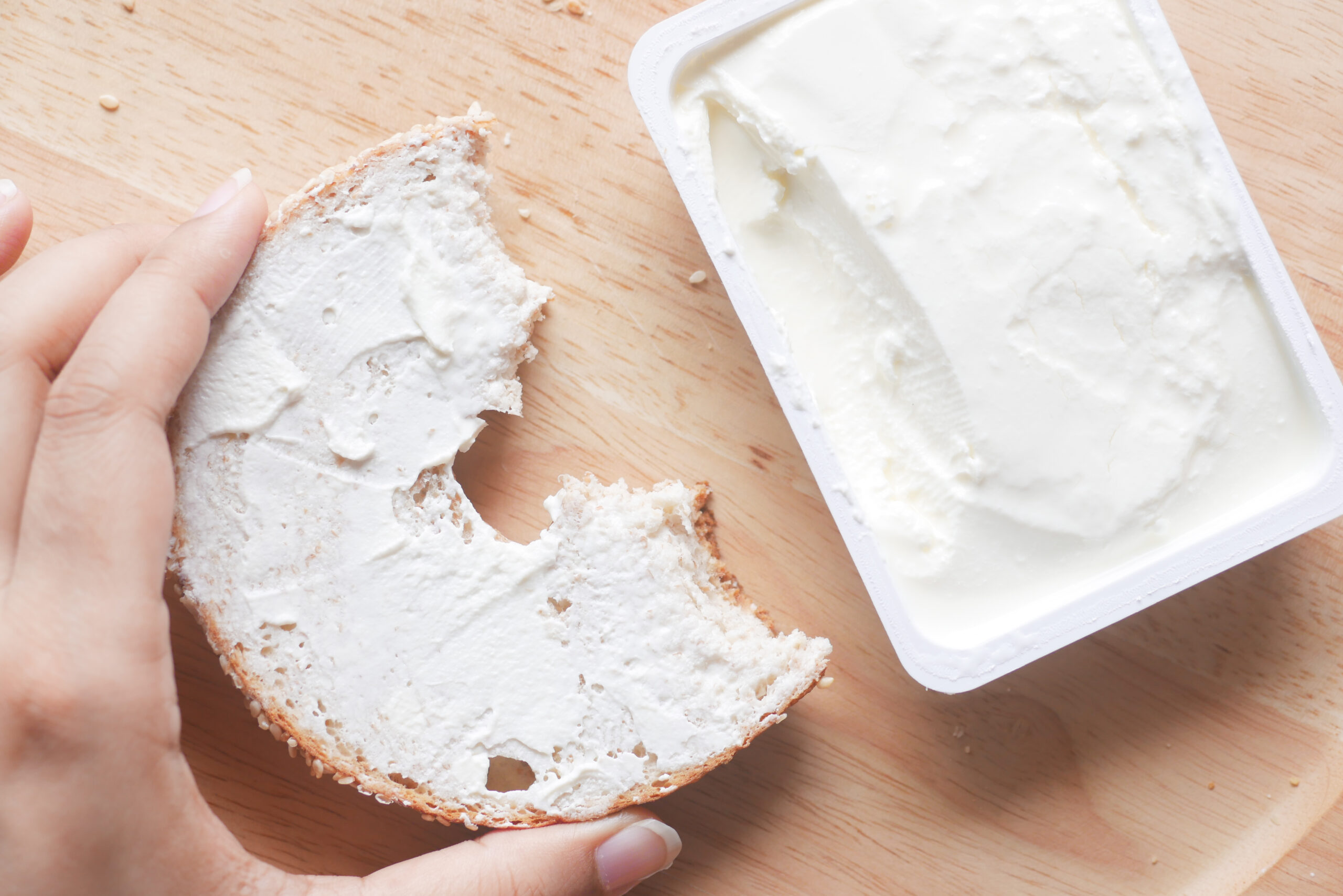 Block of cream cheese next to bagel spread with cream cheese.