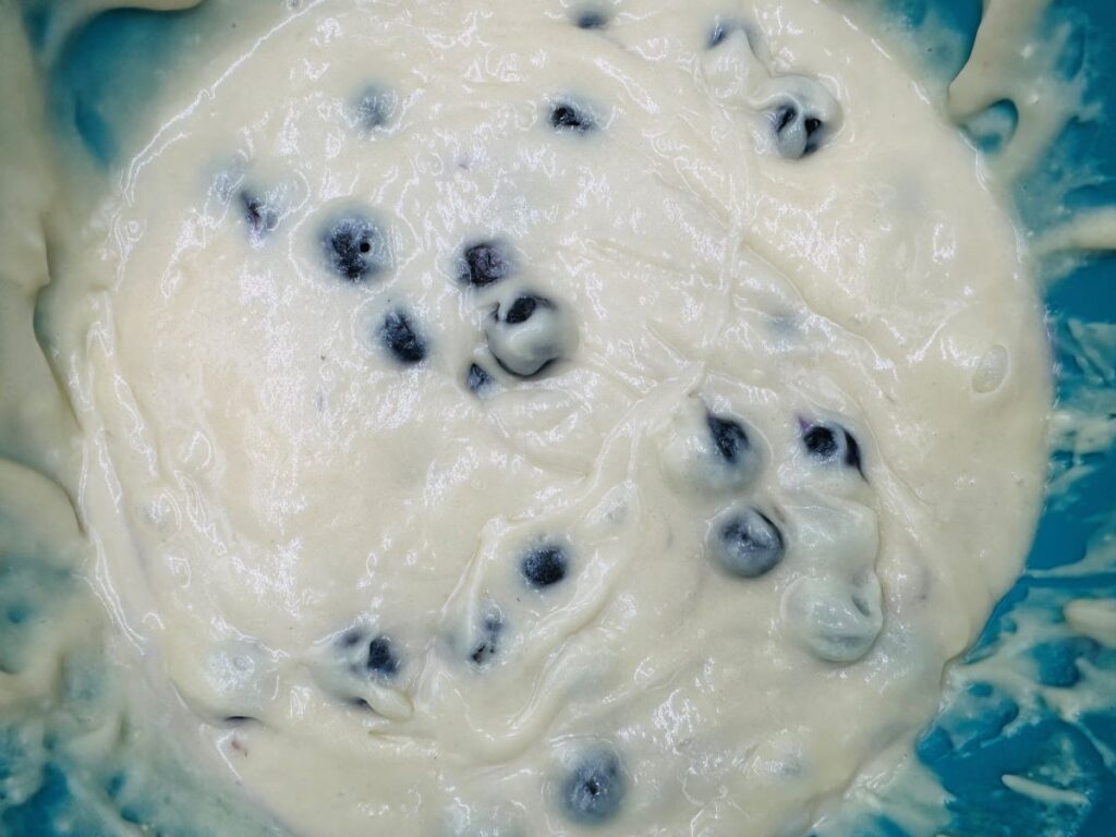 Tan batter with blueberries in teal bowl.