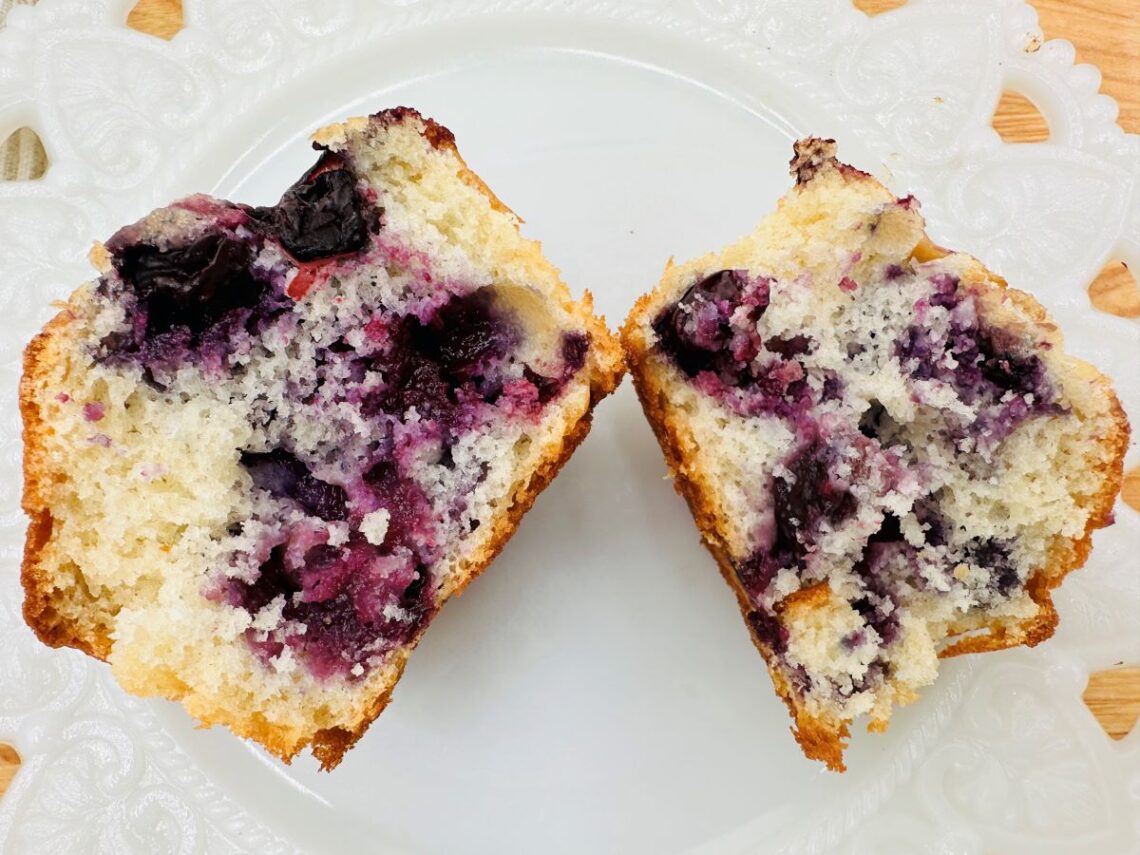 Blueberry muffin cut in half on white plate.