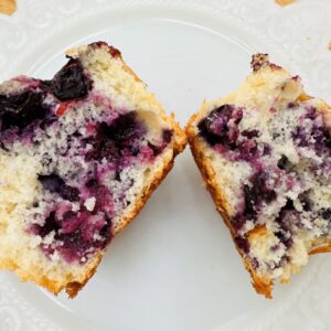 Blueberry muffin cut in half on white plate.