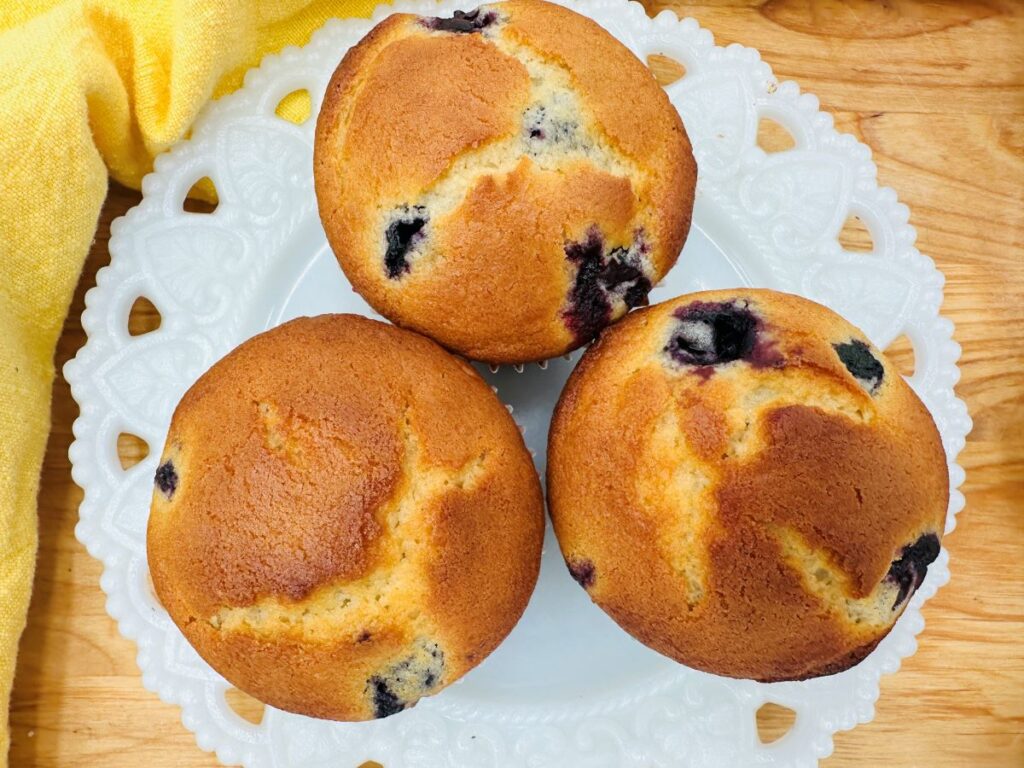 Overhead view of 3 blueberry muffins on white plate.
