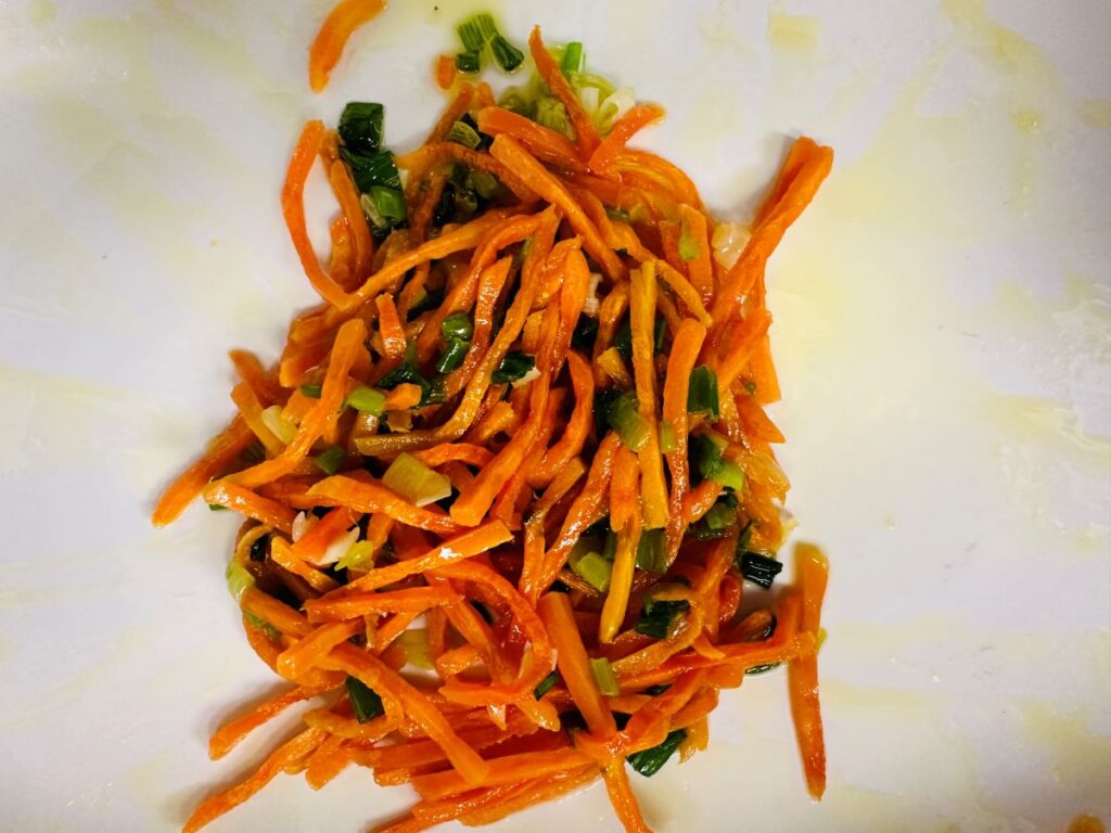 Cooked shredded carrots, green onions, and melted butter in white dish.
