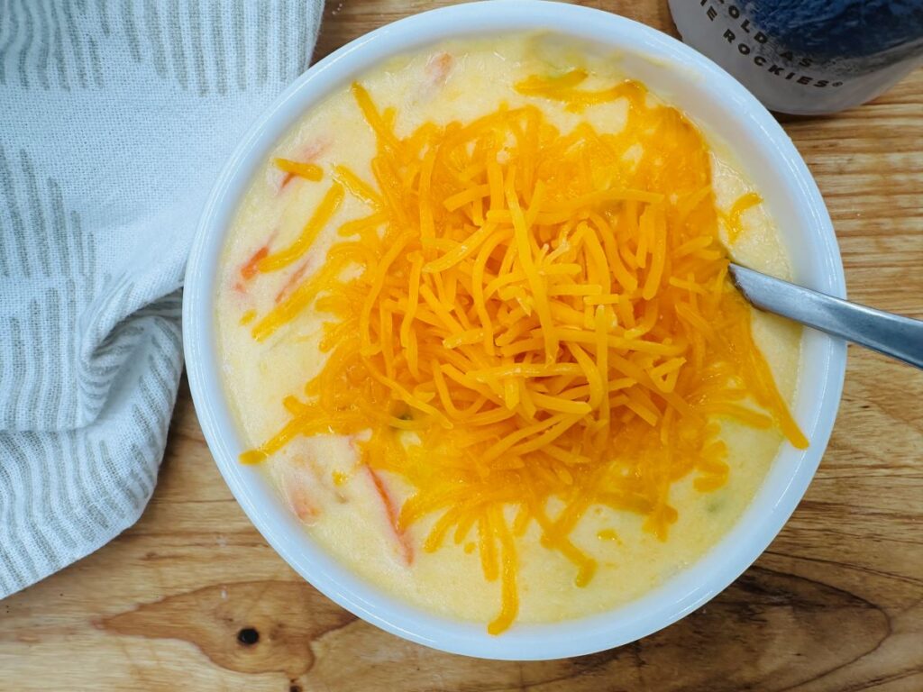 Close up of yellow soup in white bowl with shredded cheddar cheese on top.