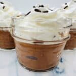 Three jars of chocolate mousse topped with whipped cream and chocolate sprinkles.
