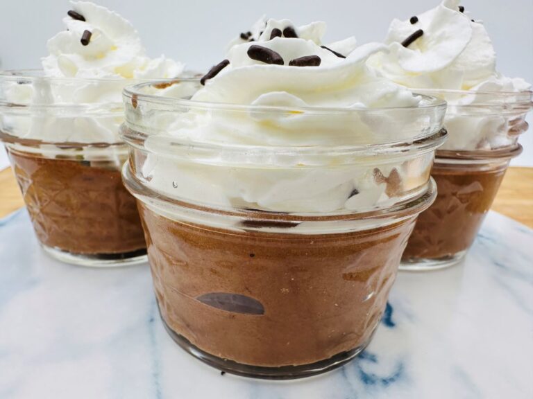 Three jars of chocolate mousse topped with whipped cream and chocolate sprinkles.