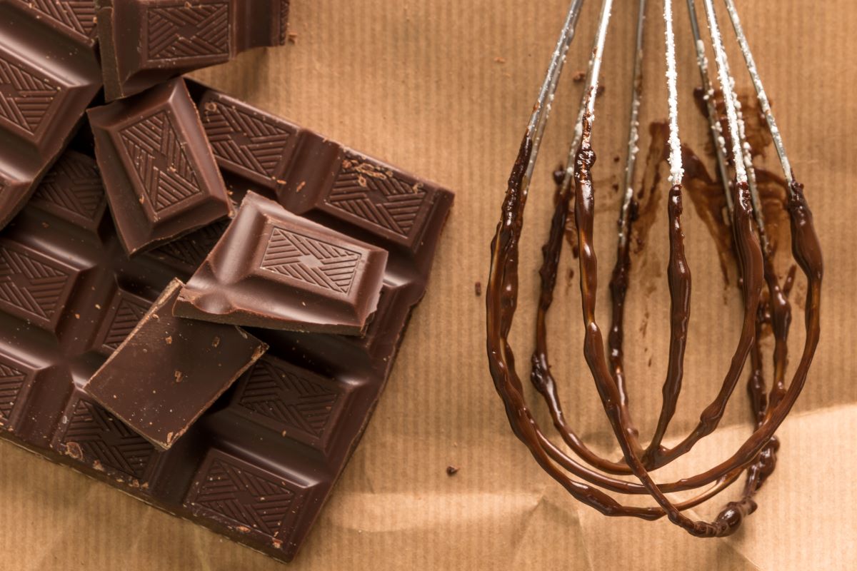 Chocolate bar next to whisk covered in melted chocolate.
