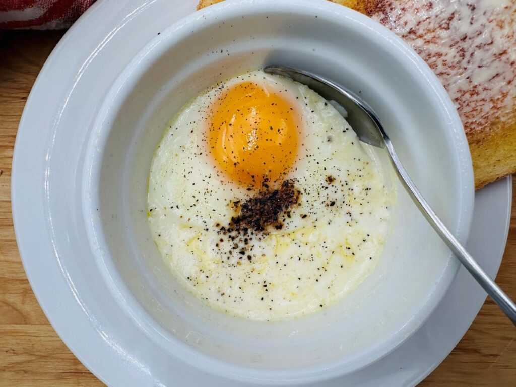 Close up of cooked egg in white bowl with spoon.