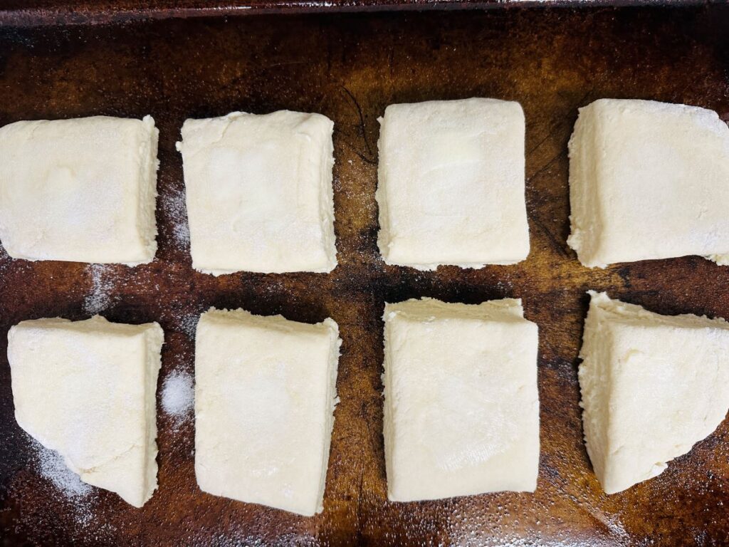 Eight square pieces of dough on cookie sheet.